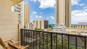 A balcony with wooden chairs, overlooking tall buildings and a clear sky.