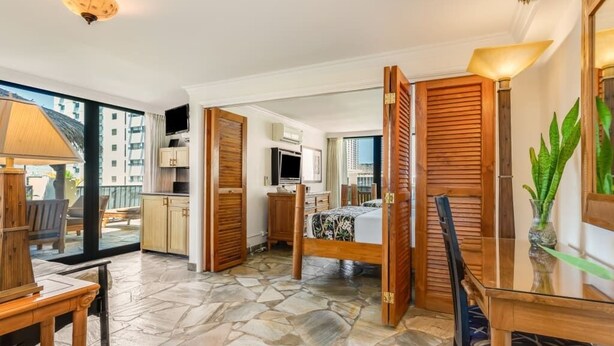 A hotel room with a stone floor, wooden furniture, a bed, a desk, and a TV.