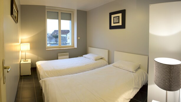 Quarto de hotel com duas camas, uma janela, um abajur e um quadro na parede.