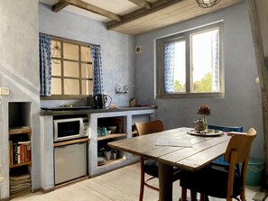 A compact kitchen with a microwave, sink, and wooden cabinets. There is a dining table with chairs and a vase with flowers. - Mediterranean apartment of Guesthouse In de Aap - Finca - Hartje Bergen (Bergen (NH))