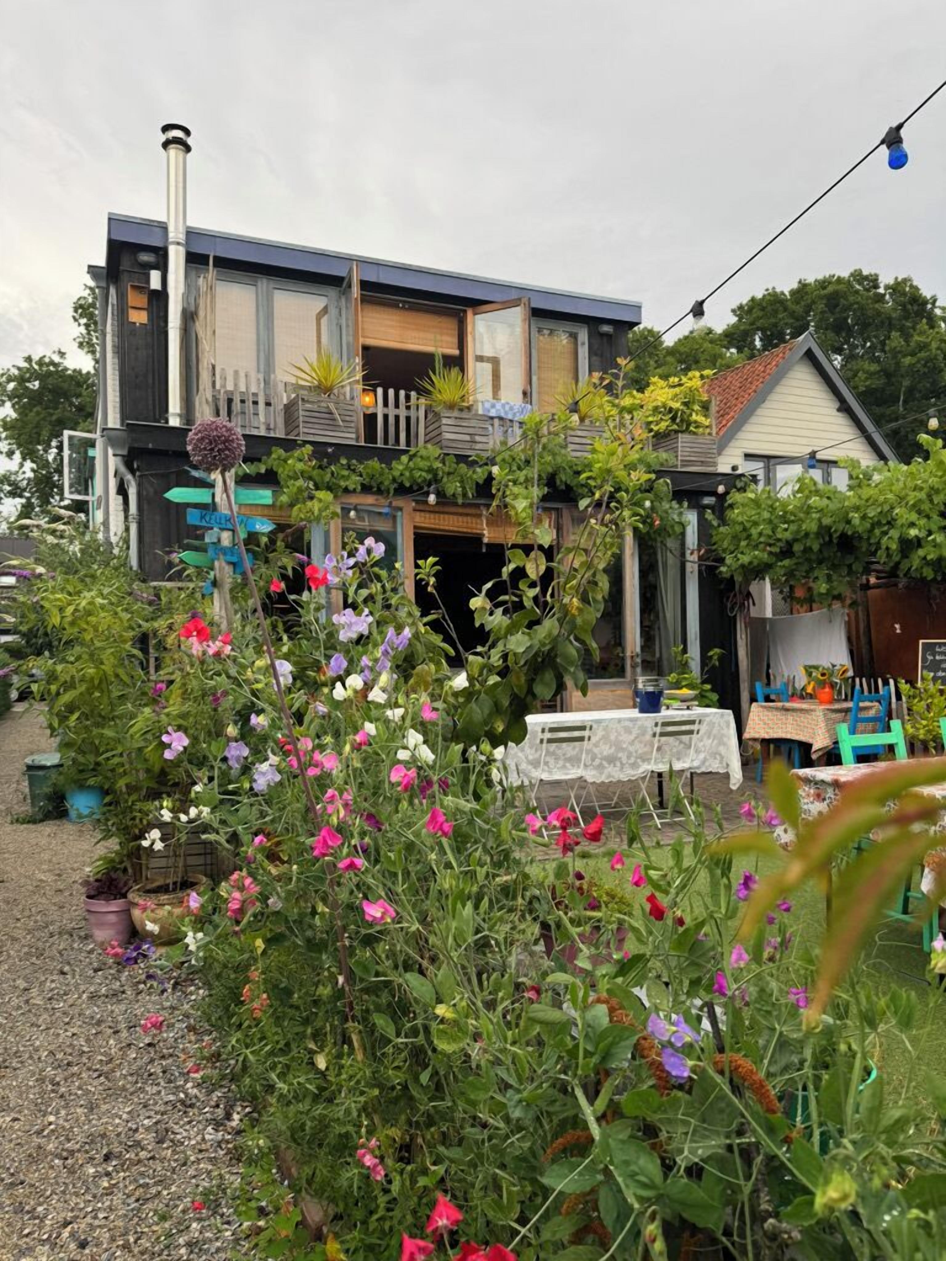 A modern house with a garden in front, a dining area with outdoor seating, and a visible chimney. - Mediterranean apartment of Guesthouse In de Aap - Finca - Hartje Bergen (Bergen (NH))