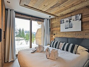A bedroom with a large bed, wooden ceiling, a painting of a bear, and a view of a snowy landscape.