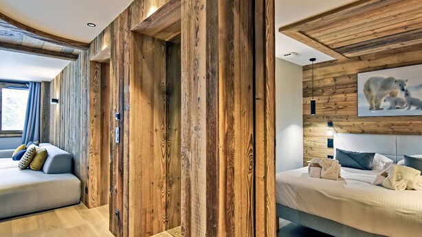 A modern interior with wooden paneling, a bed, a sofa, and a wall-mounted picture of a polar bear. - Luxury Apartment with Spa Access in Les Allues (Méribel)