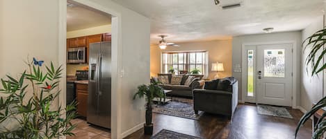 A spacious living area with a kitchen, dining area, and a front door leading to the outside.