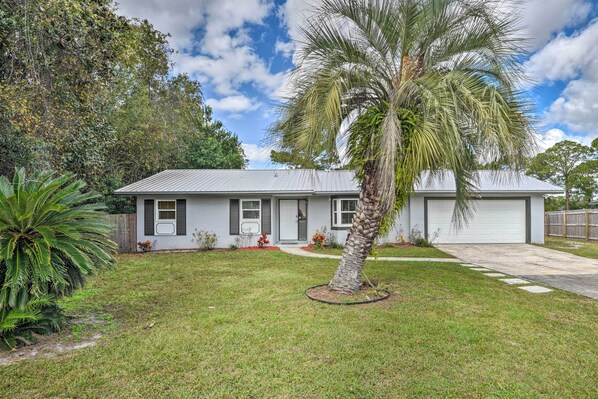 Una casa de un piso con fachada blanca, un garaje y un césped bien cuidado con una palmera.