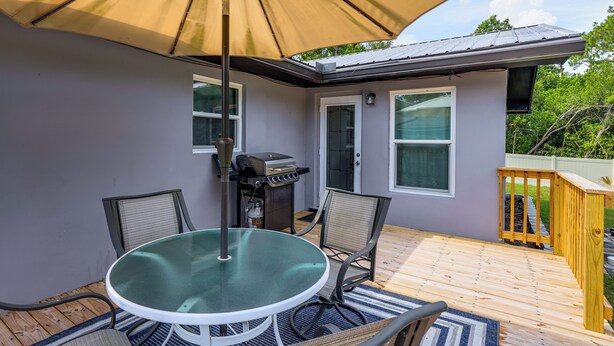 Eine Terrasse mit rundem Tisch, Stühlen, einem Grill und einem Sonnenschirm.