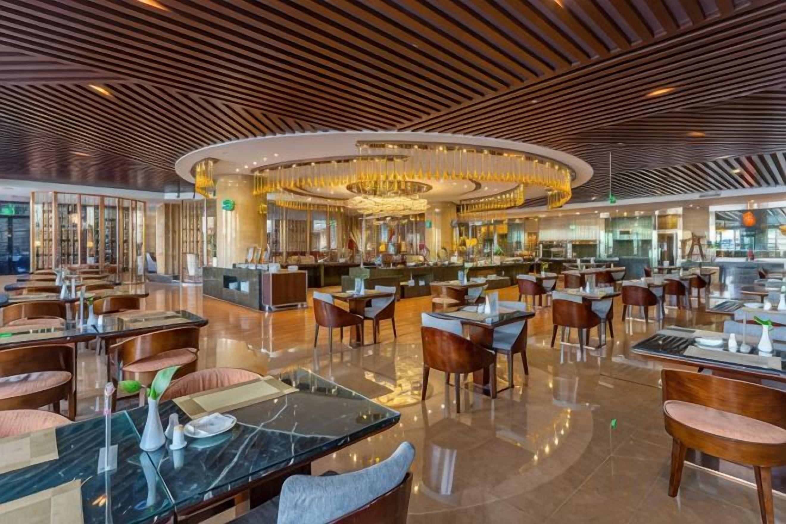 A spacious hotel lobby with a central bar area, multiple seating arrangements, and a modern ceiling design.