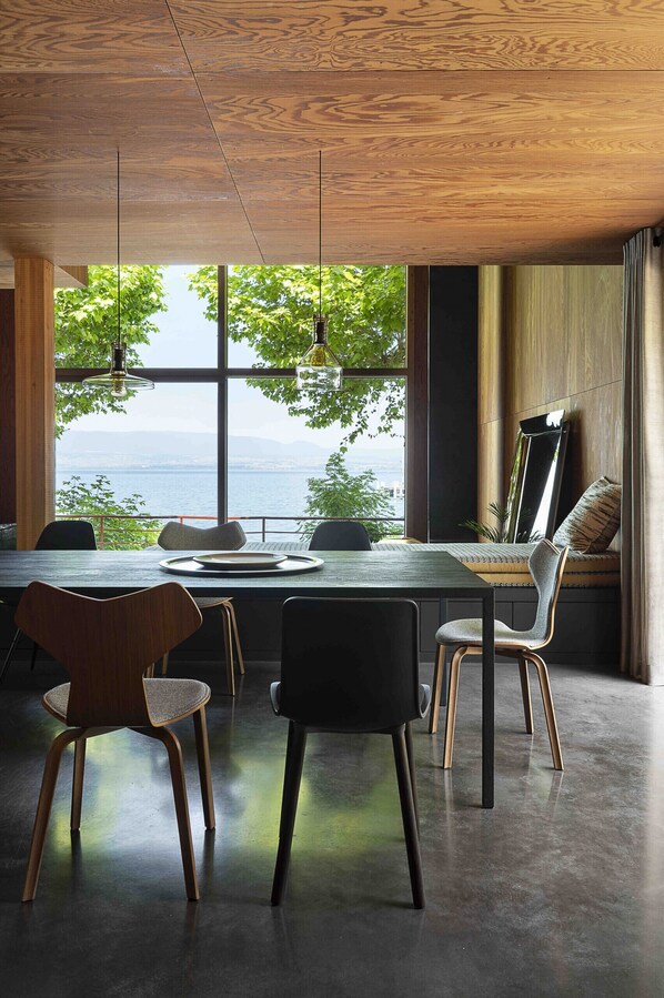 Un espace repas moderne avec vue sur la mer, un plafond en bois et de grandes fenêtres.