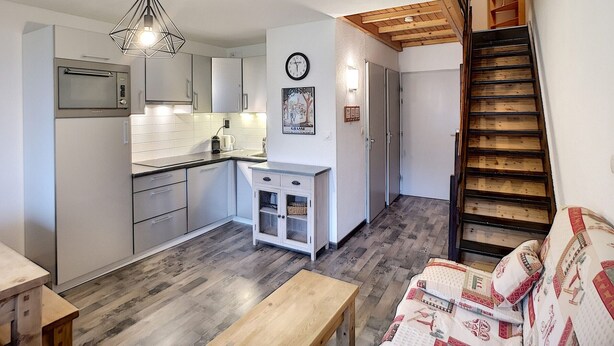 Une cuisine moderne avec des meubles blancs, un four à micro-ondes et un escalier en bois menant à une chambre à coucher située en mezzanine.