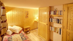 Une pièce confortable avec un lit, un petit tabouret en bois, une bibliothèque et une porte ornée d’un panneau en bois.