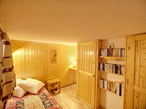 Una habitación acogedora con una cama, un taburete de madera, una estantería y una puerta con detalles de panel de madera.