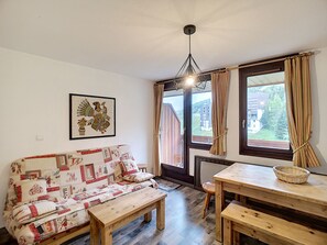 A cozy living room with a sofa, a wooden table, and a bench. There is a framed picture on the wall and a window with curtains.
