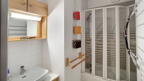 Une salle de bain avec un meuble-lavabo en bois, un miroir, un lavabo et une douche dotée d’une porte en verre.