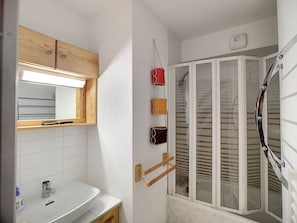 Un baño con tocador de madera, espejo, lavamanos y ducha con puerta de cristal.