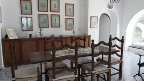 A dining area with a wooden table and chairs, a decorative cabinet, and framed artwork on the wall. - Villa Sunrise (Lacco Ameno - Forio)