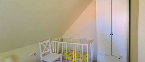 A room with a white crib, a white chair, a white nightstand, and a white wardrobe.