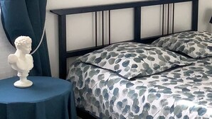 Une chambre à coucher comprenant un lit, une table de chevet, une sculpture en buste, un tableau et un luminaire au plafond.
