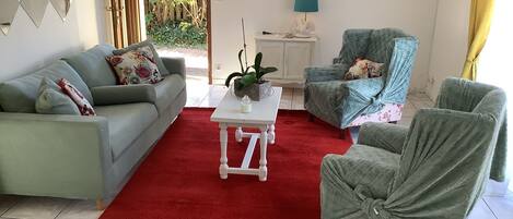 A living room with a red rug, a white coffee table, a grey sofa, a blue armchair, and a green armchair.