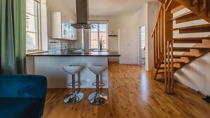 Een moderne keuken met een centraal eiland, houten vloeren en een trap met houten leuning.