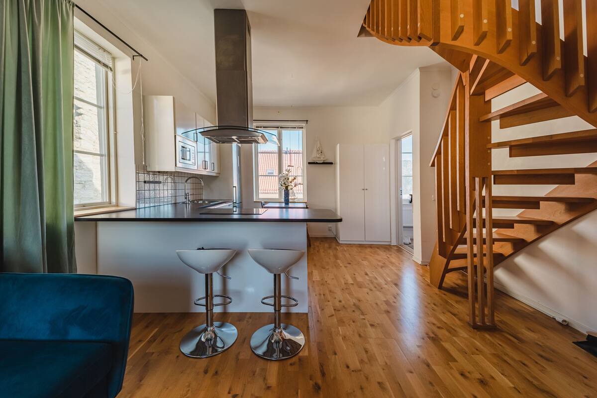 Eine moderne Küche mit einer zentralen Kochinsel, Holzböden und einer Treppe mit hölzernem Geländer.