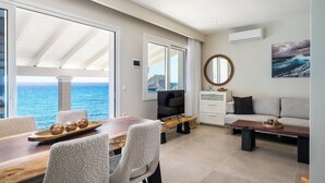 A spacious living area with a large window overlooking the sea, a cozy seating arrangement, and a flat-screen TV.