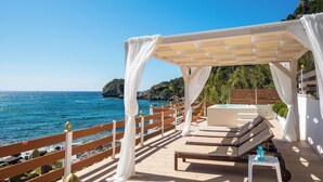 A beachside lounge area with a pergola, sun loungers, and a hot tub, overlooking the sea.