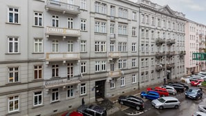 Un edificio de varios pisos con balcones, un estacionamiento con diversos automóviles y una acera para peatones.