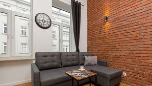 Una sala de estar moderna con un sofá gris, una mesa de centro de madera, un reloj y una pared de ladrillo.