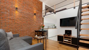 Una sala de estar moderna con pared de ladrillo, sofá gris, piso de madera y televisor montado en la pared.