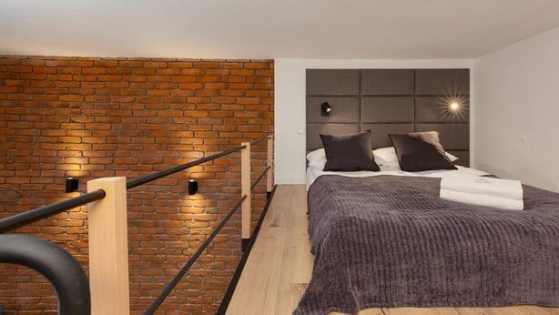 Un dormitorio moderno con pared de ladrillo, una cama con cabecero y barandilla de madera.