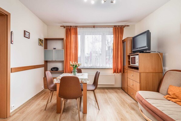 A compact living space with a dining table, chairs, a sofa, a television, and a window with curtains.