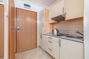 A compact kitchen with wooden cabinets, a stainless steel sink, and a kettle on the countertop.