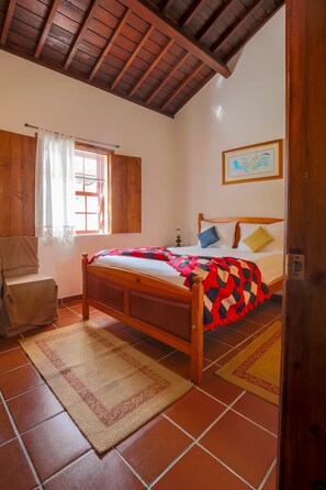 A bedroom with a wooden bed, a window with curtains, a framed picture on the wall, and a door.