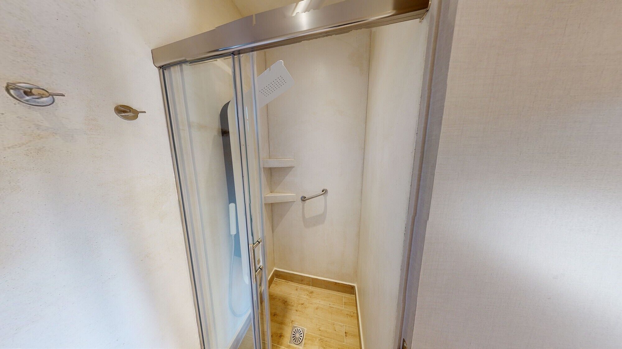 Ducha con puerta de vidrio, barra para toallas y un estante pequeño.