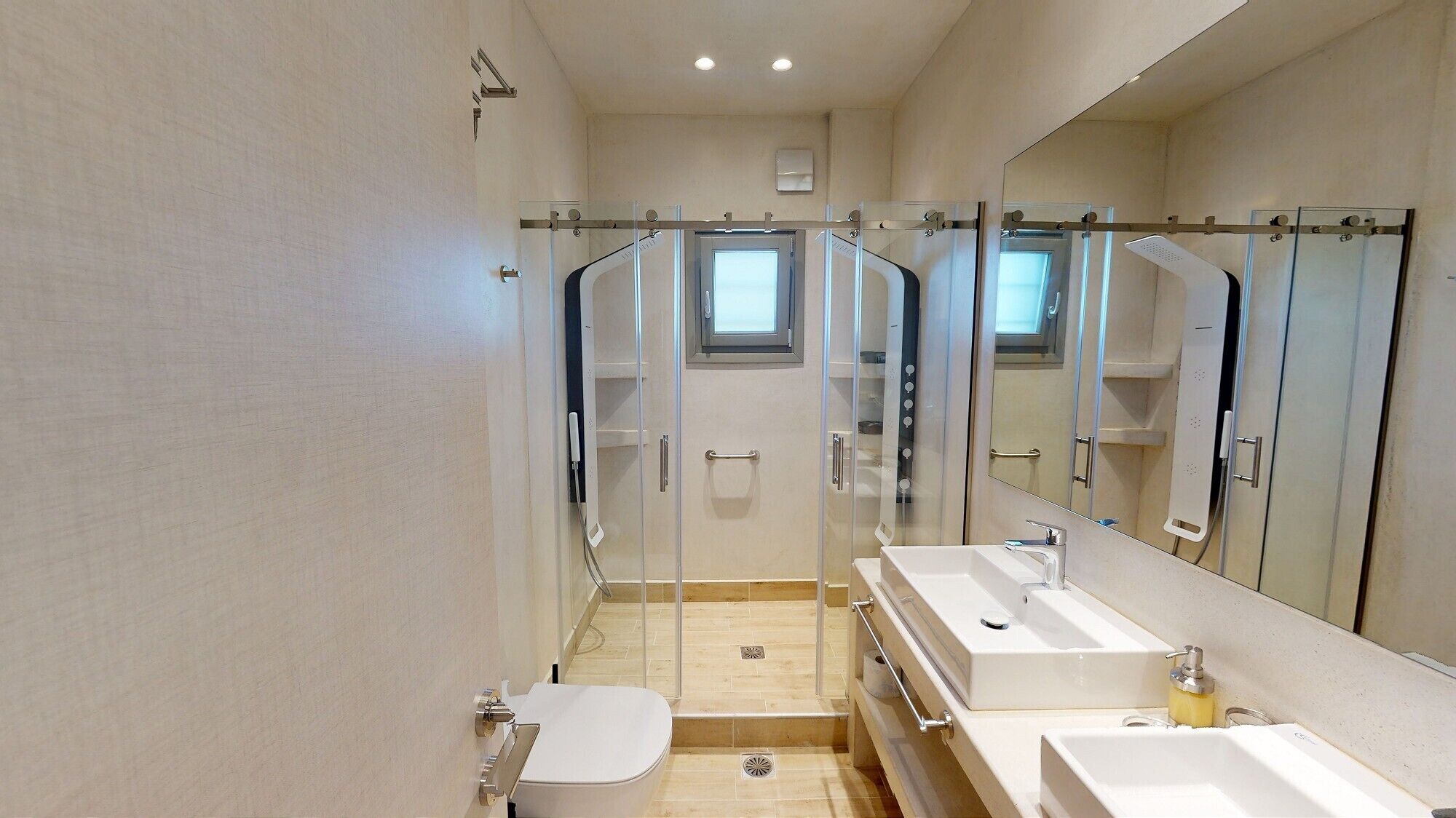 Un baño moderno con ducha envuelta en vidrio, un espejo grande y dos lavamanos.