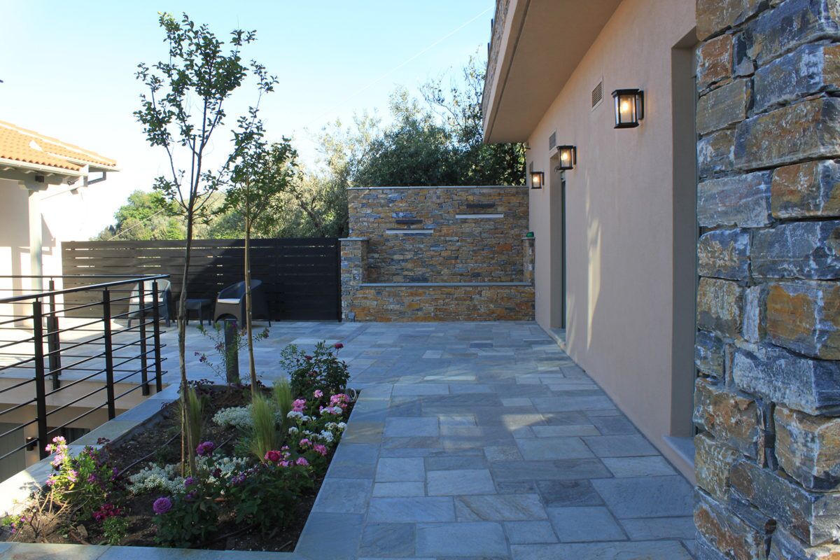 A modern outdoor patio with stone flooring, a low stone wall, and a metal railing.