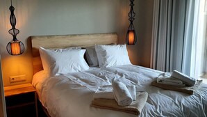 Una cama bien hecha con sábanas y almohadas blancas, cabecera de madera y dos lámparas colgantes.