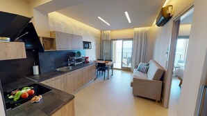 Una cocina moderna con horno empotrado, una zona de comedor con mesa y sillas, un sofá y un balcón con cortinas.