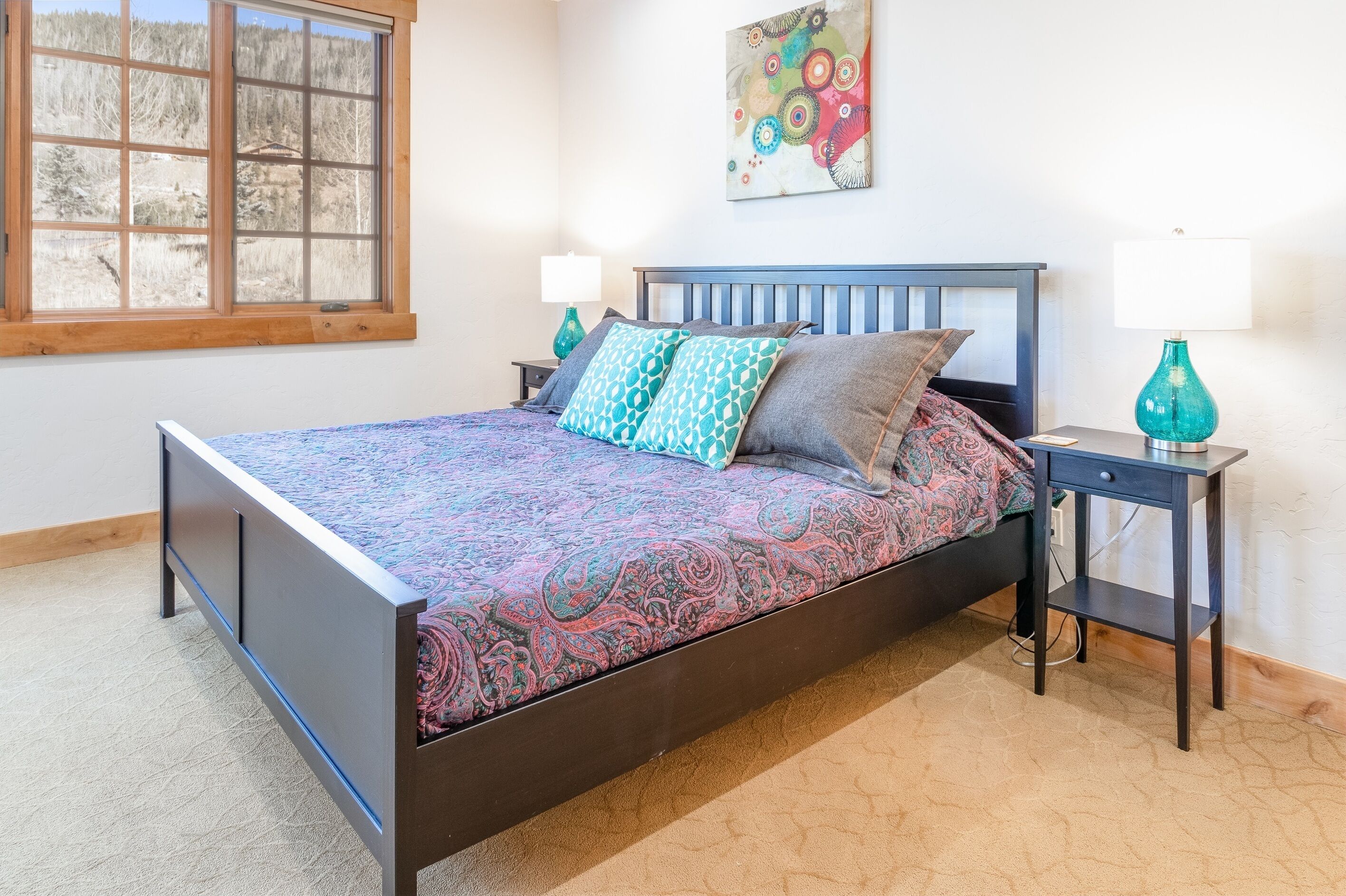 A bedroom with a bed, two nightstands, a window, and a wall-mounted artwork.