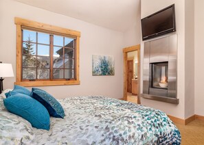 Un dormitorio con una cama grande, una ventana, un cuadro, una chimenea y un televisor.