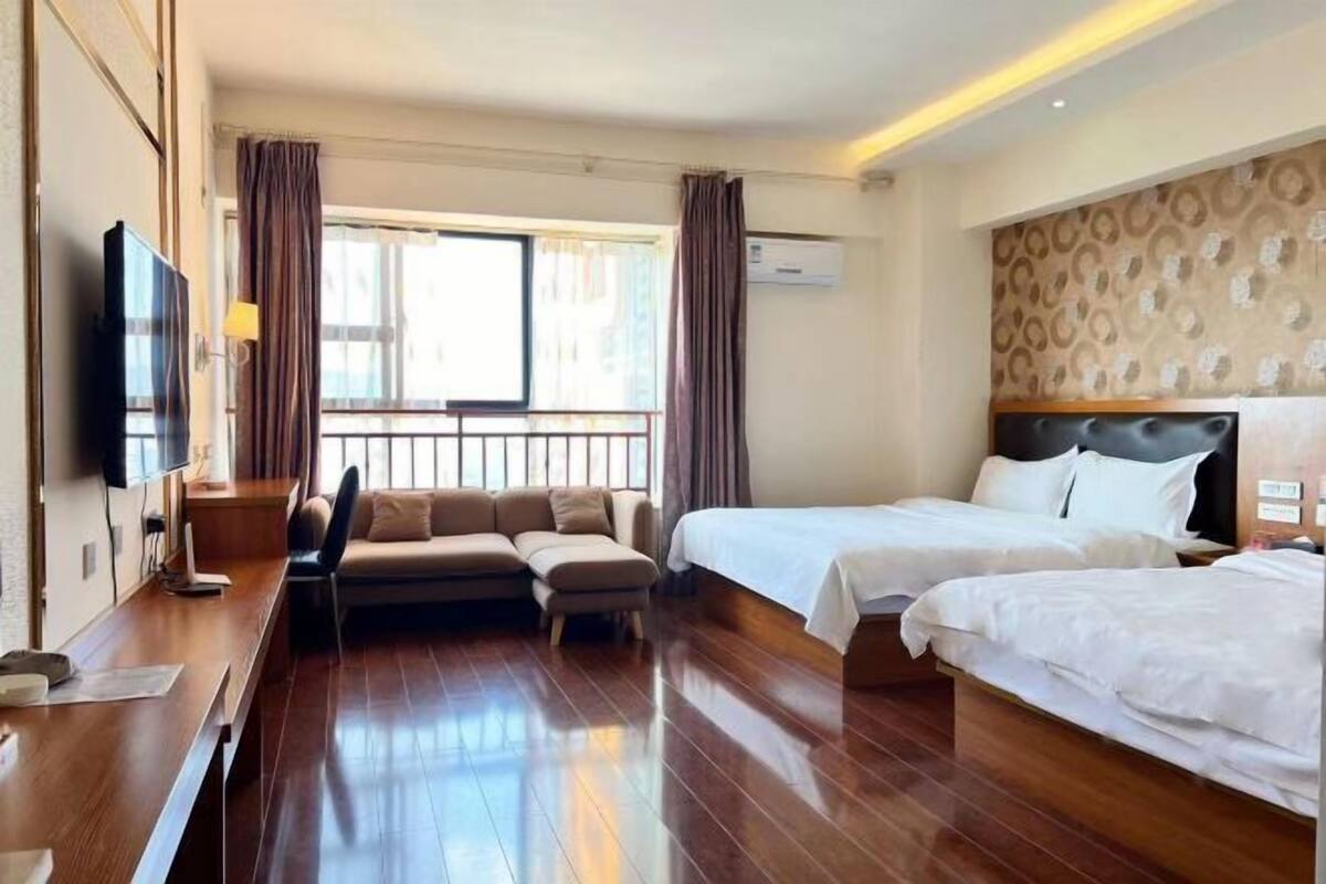 Ein Hotelzimmer mit Holzboden, einer Couch, zwei Betten, einem Fernseher und einem Fenster mit Vorhängen.