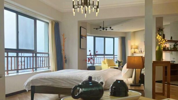 A hotel room with a bed, a dining table with a teapot and a plate of food, a lamp, and a view of the outside through large windows. - Shilin Slowly Boutique Hotel (Shilin)