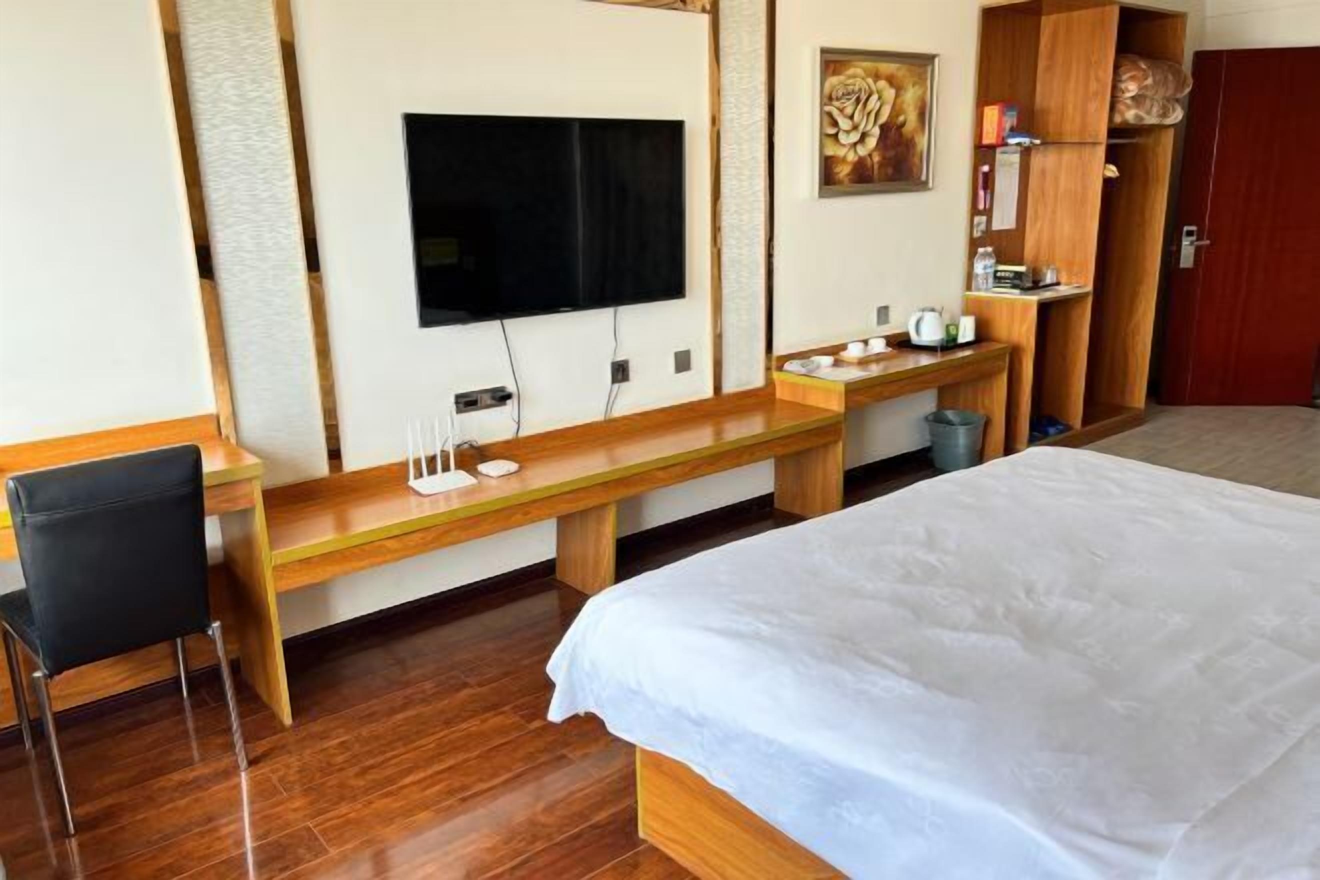 A hotel room with a bed, a desk with a chair, a TV, and a wardrobe.