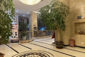 A lobby with a large potted plant, a glass railing, and a tiled floor.