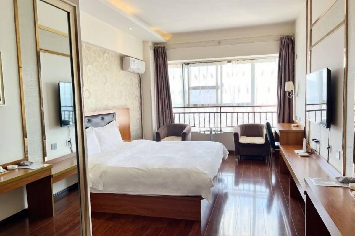 Ein Hotelzimmer mit einem großen Bett, einem Schreibtisch, einem Stuhl, einem Fernseher und einem Fenster mit Vorhängen.