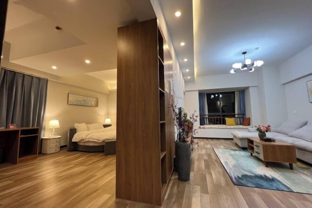 Ein modernes Hotelzimmer mit Holzboden, einem Bett, einem Schreibtisch, einer Couch und einem großen Fenster mit Blick.