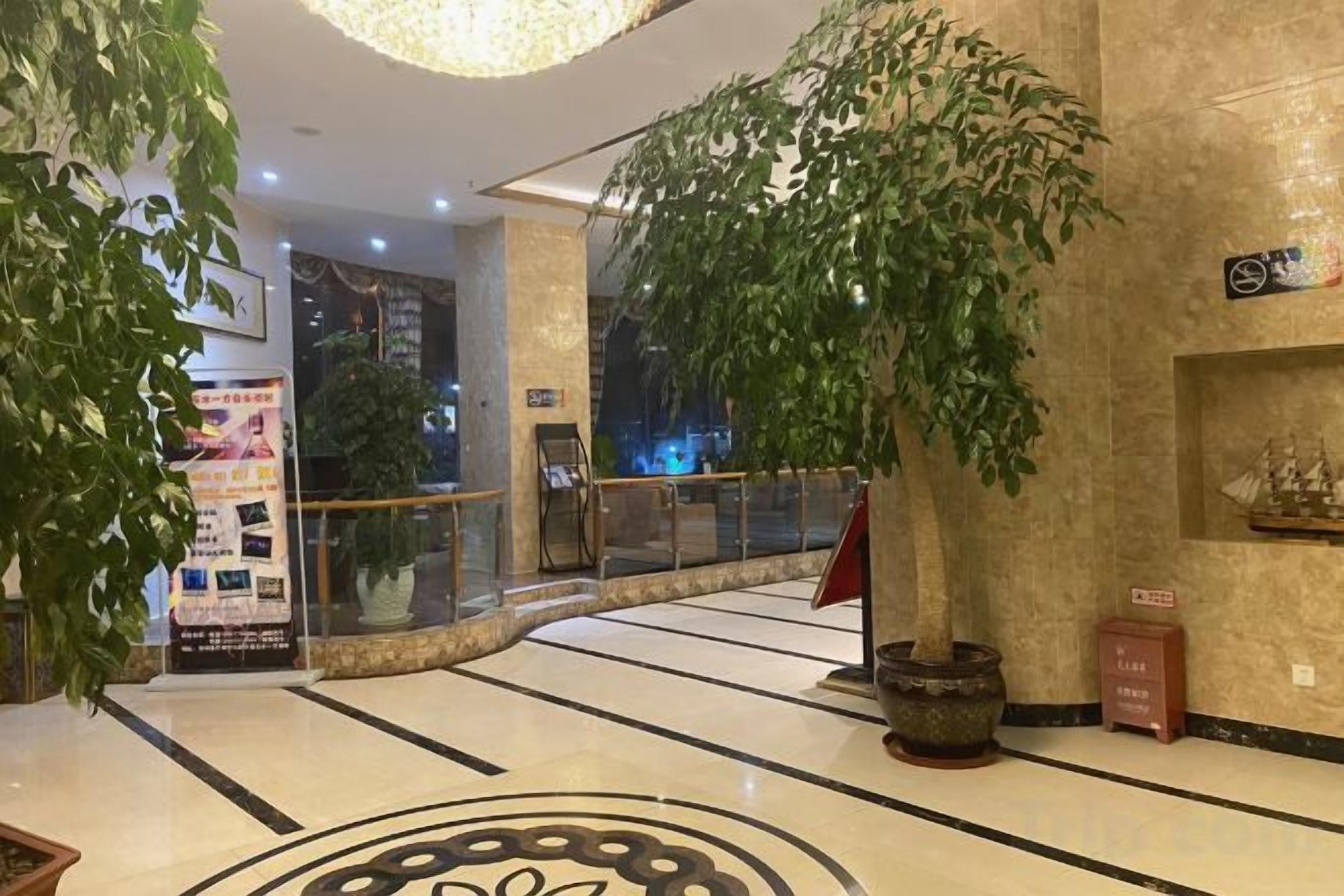 A hotel lobby with a marble floor, a large potted plant, a glass railing, and a sign on the wall.