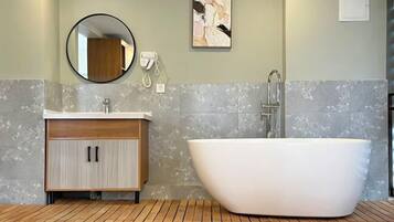 A modern bathroom with a freestanding bathtub, a wooden vanity with a mirror, and a wall-mounted telephone.