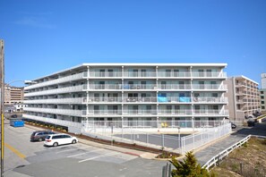 A multi-story hotel with balconies, a parking lot, and a fenced area. - Traditional, stylish 2 bedroom oceanfront condo with free WiFi, and outdoor pool, and a stunning ocean view located in quiet midtown near mini golf and bowling and just steps from the beach! (Ocean City)