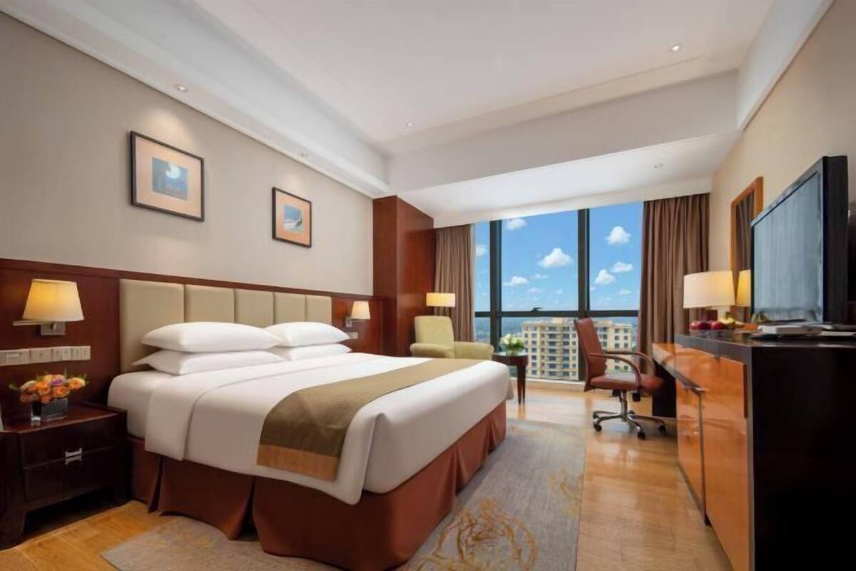 Habitación de hotel con una cama grande, un escritorio, una silla, un televisor y vistas de la ciudad.